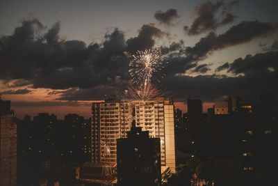 Firework display in city against sky at night