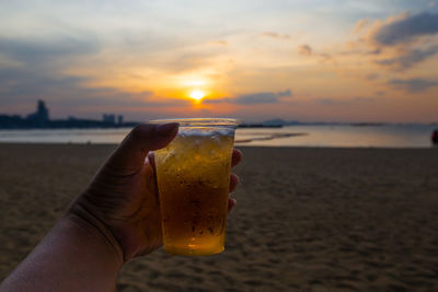 Close-up of hand holding drink at sunset