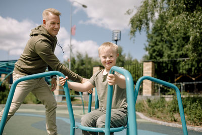 Father spinning son with down syndrome on carousel at park during sunny day