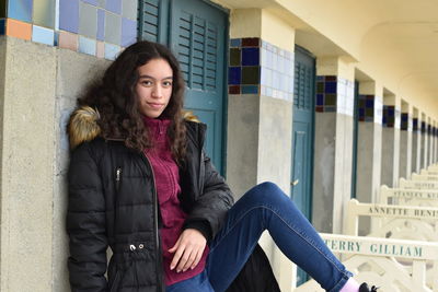 Portrait of girl wearing warm clothing while sitting against building