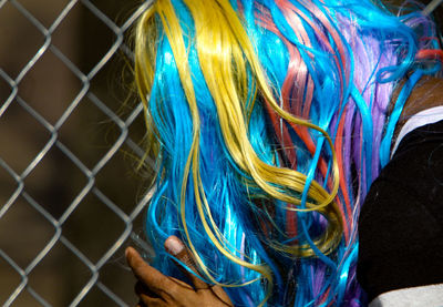 Close-up of person wearing multi colored wig against fence