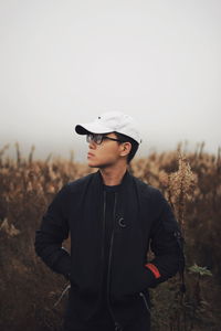 Young man wearing hat standing on field against sky