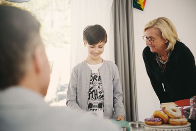 Smiling boy looking at birthday present while standing with grandmother at table