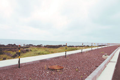 Delineator pole in row by sea against cloudy sky