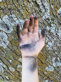 Close-up of cropped dirty hand against tree trunk with lichens