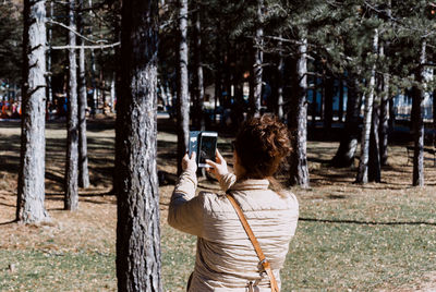 Rear view of woman photographing with mobile phone in forest
