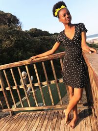 Young woman standing on railing against sky