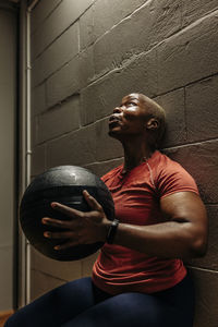 Dedicated female athlete holding medicine ball while doing wall sit exercise at gym