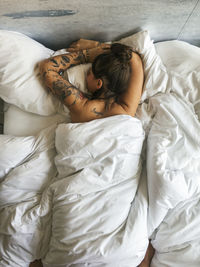 Directly above shot of tattooed woman covered with duvet while lying on bed