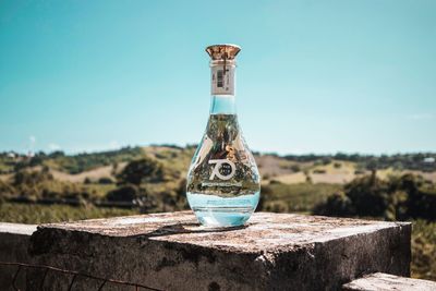 Close-up of glass bottle on table against blue sky