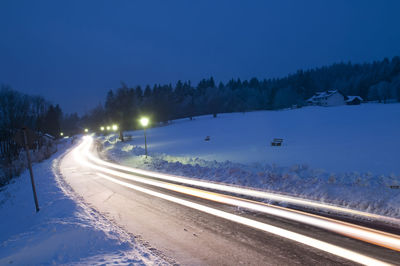 Light trails on road against clear blue sky at night