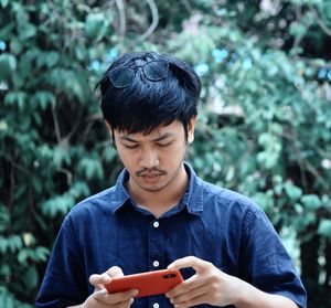 Young man using smart phone while standing against trees