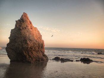 Rock formation on beach against sky during sunset