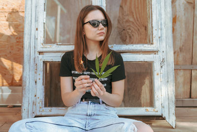 Young woman holding illuminated sparkler while sitting on wood