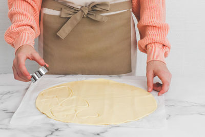 Young caucasian girl baker in an apron in the process of cutting out a metal heart shape raw dough