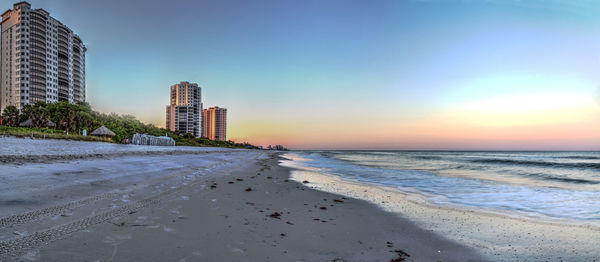 Scenic view of beach and buildings against sky during sunset