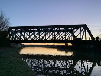 Silhouette bridge over river against clear sky