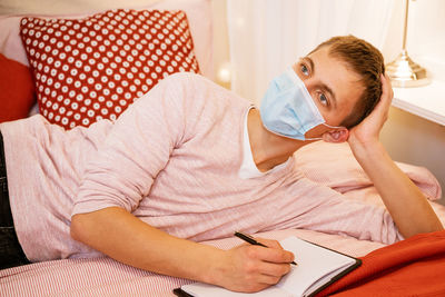 A man in a protective mask lies with a notebook and writes