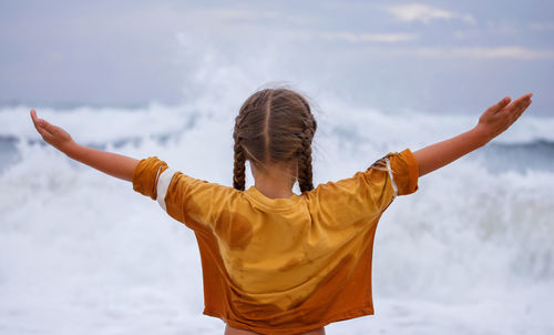 Young man with arms raised standing against sky