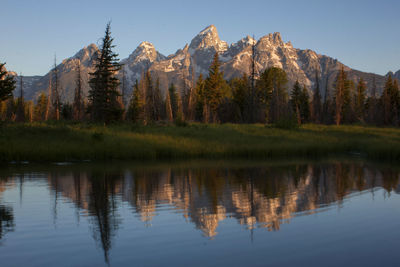 Reflection of trees in calm lake in front of mountains