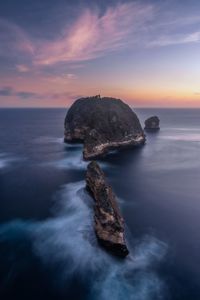 Rock formation in sea against sky during sunset