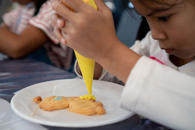 Cute girl decorating cookie with icing in plate on table