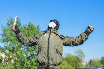 A thug in a balaclava with a knife raises his hands