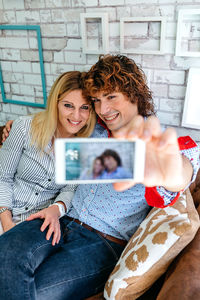 Man taking selfie with girlfriend from mobile phone while sitting on sofa