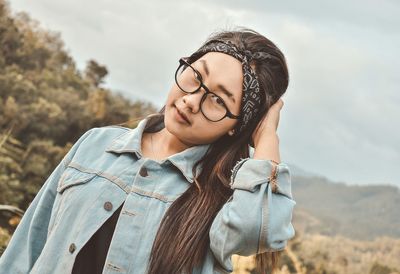 Portrait of woman wearing denim jacket standing against sky