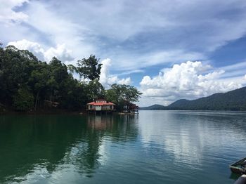 House by lake and buildings against sky