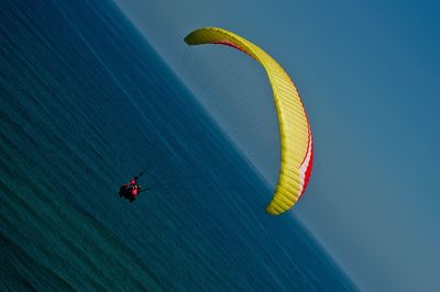 Person paragliding over sea against clear blue sky