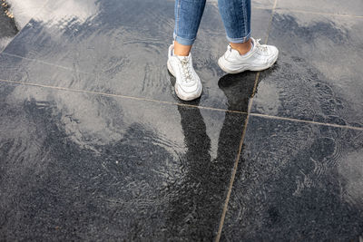 Low section of woman standing on wet footpath