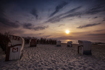 Hooded beach chairs on sand against sky during sunset