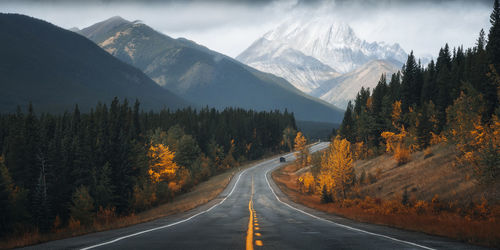 Road amidst trees and mountains against sky