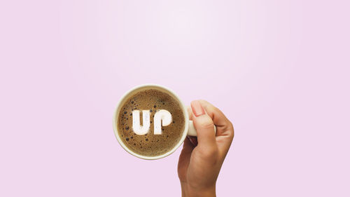 Close-up of hand holding coffee cup against white background