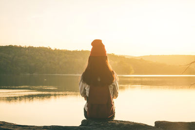 Rear view of woman sitting by lake against clear sky