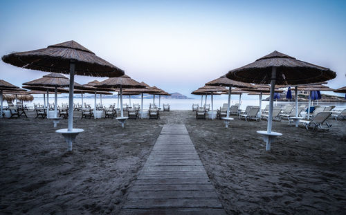 Parasols and lounge chairs at beach against clear sky