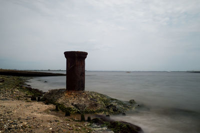 Rusty metal column at sea shore against sky