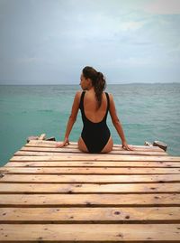 Full length of woman sitting on pier at beach against sky