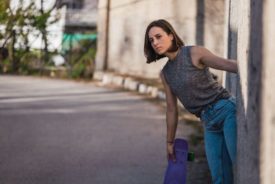 Portrait of young woman holding skateboard by road