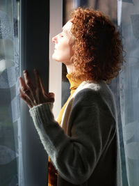 Side view of woman with eyes closed sunbathing through window at home
