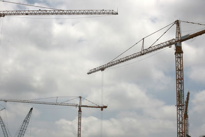 Low angle view of cranes against cloudy sky