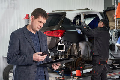 Businessman standing while mechanic working in background