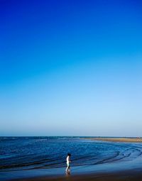 Girl walking on beach against clear blue sky