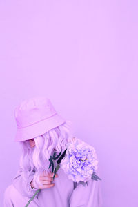 Woman wearing hat holding flowers standing against colored background