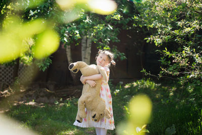 Cute european kid girl in dress with soft big toy dog in backyard, in park summer