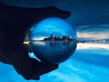 Close-up of hand on sea water against cityscape