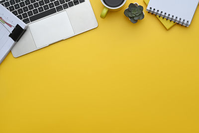 Directly above shot of laptop and headphones on yellow background