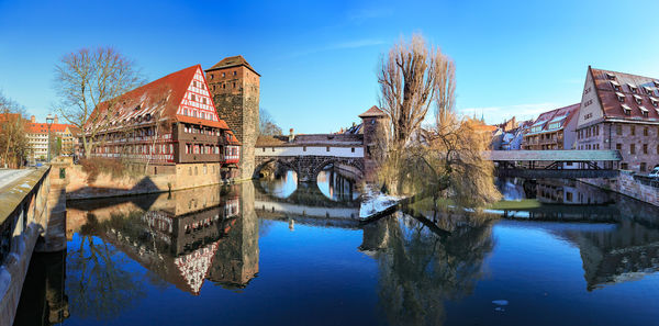 Arch bridge over river by buildings against blue sky