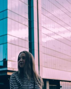 Low angle view of thoughtful beautiful woman standing against modern building